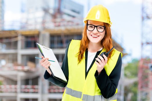 Woman builder in protective clothes at construction site walkie-talkie