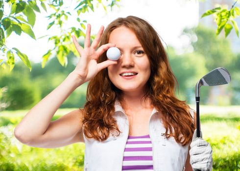 Beautiful girl with red hair and a golf ball on a background of golf courses