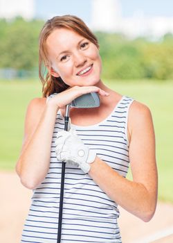 Cute girl with a golf club on a background of golf courses in a striped T-shirt