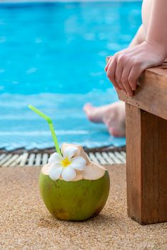 woman in a lounger near the pool and a coconut with a straw near her close-up