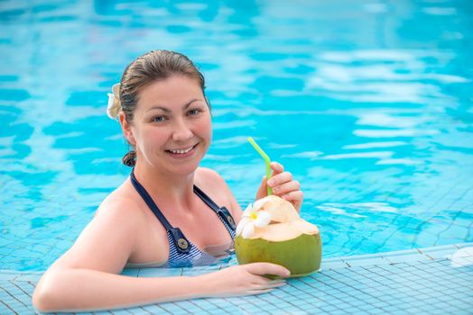 happy brunette with coconut resting in the pool in the tropics