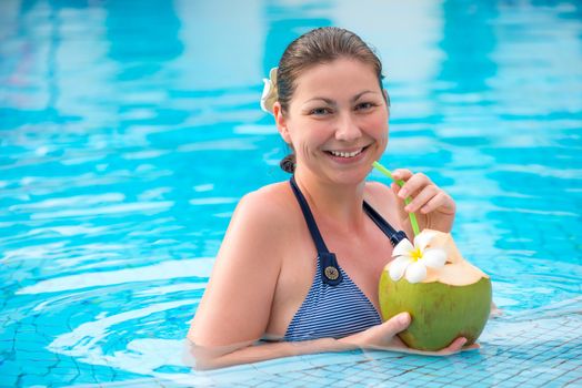portrait of a woman with a coconut resting in a pool in the tropics