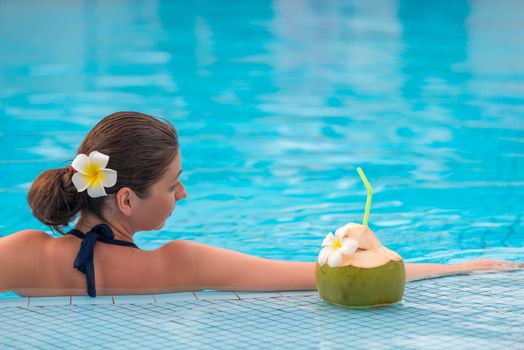 relaxing woman in a bikini in a pool with a juicy coconut