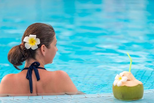 brunette relaxes in the pool, standing near a coconut with a straw