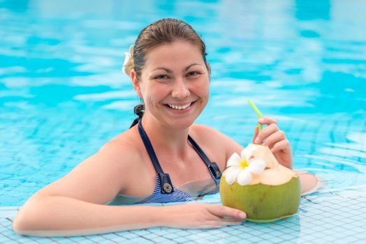 beautiful young woman enjoys delicious coconut milk while in the pool