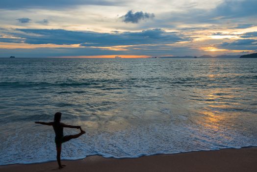 active woman doing yoga on the beach at sunset time