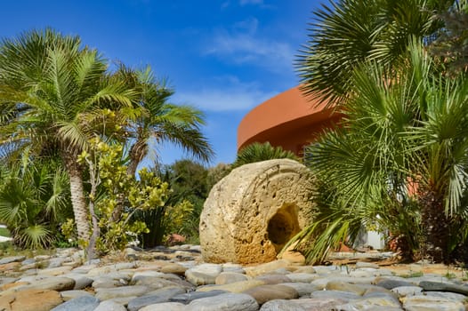 Old press wheel serving as a garnish in a pebble and palm grove in Maleme in western Crete