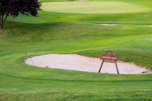 Chipping green sign in front of bunker on golf course, detail of golf ground