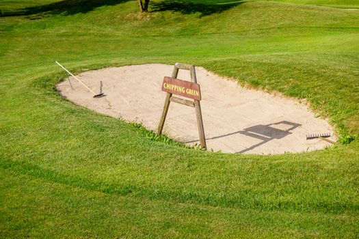 Chipping green sign in front of bunker on golf course, detail of golf ground