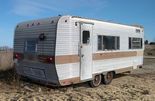 An old white and tan recreational vehicle trailer parked in a country field.