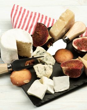 Arrangement of Gourmet Cheese with Brie, Parmesan, Roquefort and Camembert and Figs with Biscuits on Slate Plate closeup on Wooden background