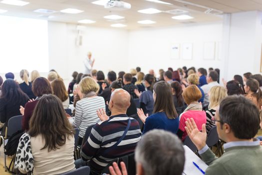 Life coaching symposium. Female speaker giving interactive motivational speech at entrepreneurship workshop. Audience in conference hall. Rear view of unrecognized participant.