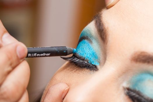 Makeup artist applying blue eyeshadow on white woman eyes