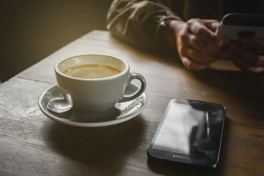 Empty coffee latte mug on wooden table, With hand woman relaxing time in phone
