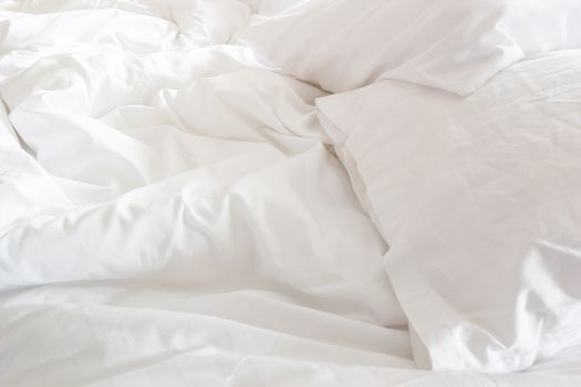 wrinkle messy blanket and white pillow in bedroom after waking up in the morning, from sleeping in a long night, details of duvet and blanket, an unmade bed in hotel bedroom with white blanket.