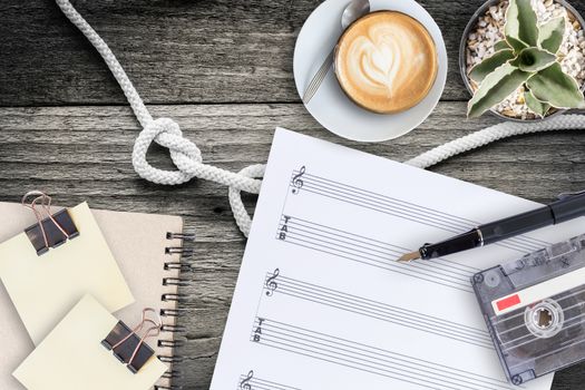 Sheet music, cactus, fountain pen, tape cassette and coffee latte on vintage wooden table