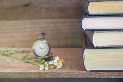 stack of thick books with pocket watch on vintage wooden wall background