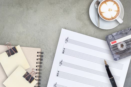 Sheet music, fountain pen, tape cassette and coffee latte on wooden table, top view picture