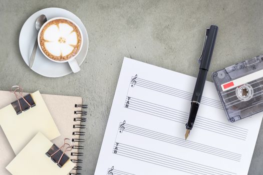 Sheet music, fountain pen, tape cassette and coffee latte on wooden table, top view picture