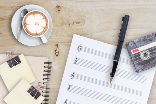 Sheet music, fountain pen, tape cassette and coffee latte on wooden table, top view picture