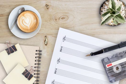 Sheet music, cactus, fountain pen, tape cassette and coffee latte on wooden table, top view picture