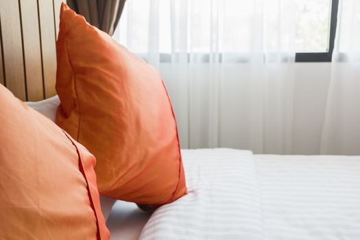 orange pillow and white blanket on bed in bedroom with lighting upper right side