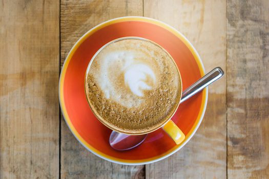 orange cup of coffee latte art with leaf pattern on wooden background, Close up of art coffee in morning