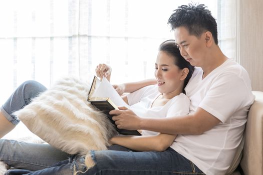 Young Couples reading book tohether in living room of contemporary house for lifestyle concept