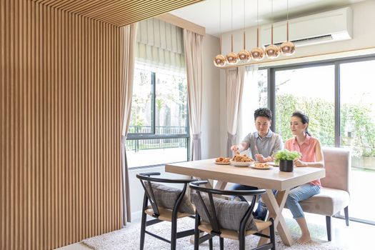 Young Asian Couples eating fried chicken together in living room of contemporary house for modern lifestyle concept