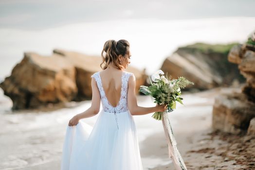 bride with a wedding bouquet on the shore of the black sea in the sunset light