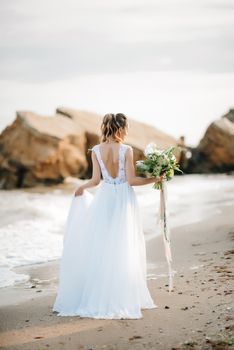 bride with a wedding bouquet on the shore of the black sea in the sunset light