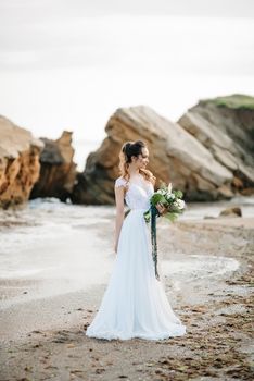 bride with a wedding bouquet on the shore of the black sea in the sunset light