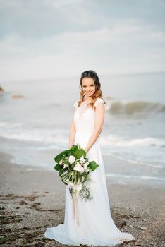 bride with a wedding bouquet on the shore of the black sea in the sunset light