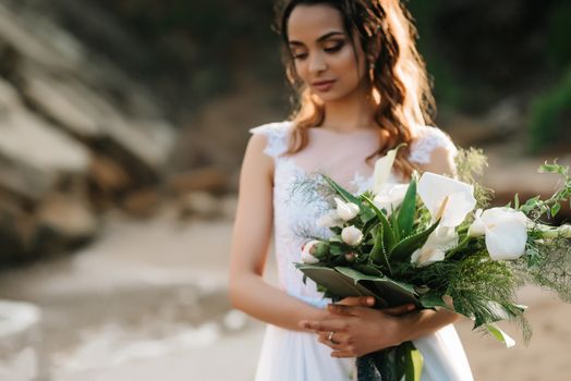 bride with a wedding bouquet on the shore of the black sea in the sunset light