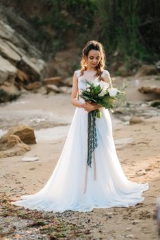 bride with a wedding bouquet on the shore of the black sea in the sunset light