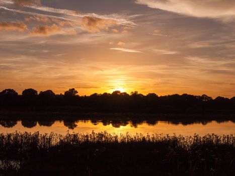 stunning bright autumn harvest sun set scene over lake water reflection reed silhouette; Essex; England; UK