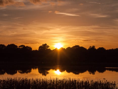 stunning bright autumn harvest sun set scene over lake water reflection reed silhouette; Essex; England; UK