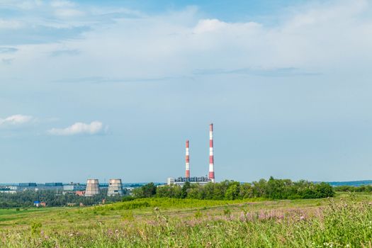 The green field and the plant with pipes on the horizon