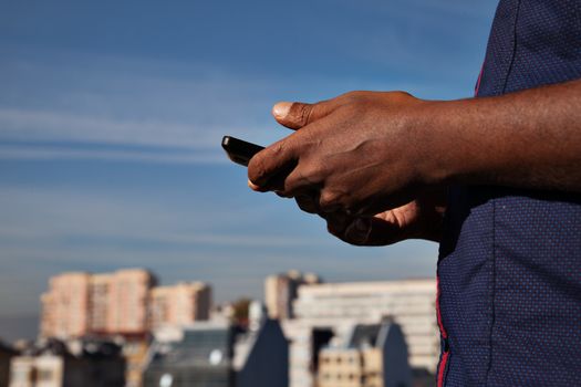 black man's hands holding phone above a cityline