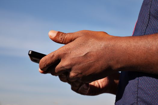 black men's hands holding phone blue sky behind