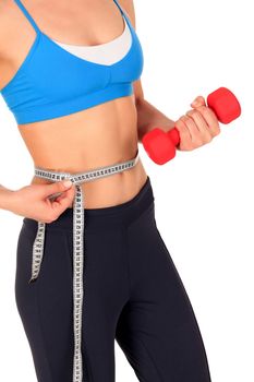 Closeup shot of slim young woman holding red dumbbell and measuring her thin waist with a tape measure, isolated on white background