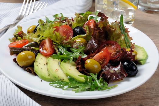 Summer salad - with avocado, olives, tomatoes in lettuce dressed, mustard-garlic sauce