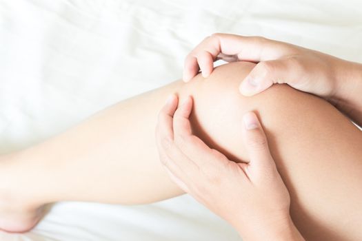 Closeup woman hand holding knee with pain on bed, health care and medical concept