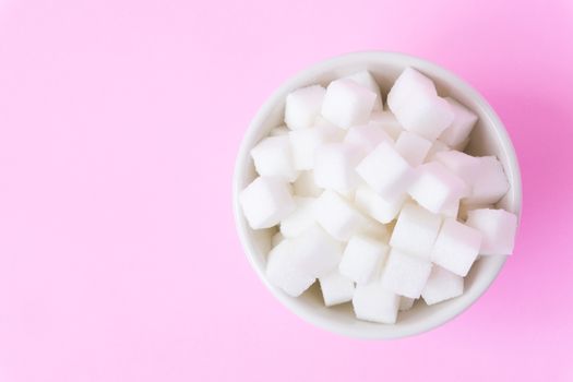 Closeup sugar cubes on bowl with pink background, health care concept