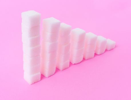 High to low stacks of sugar cubes with pink background, health care diet concept