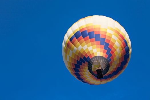 Colorful hot-air balloon in flight seen from below against a blue sky