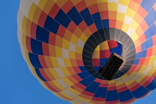Closeup of a colorful hot-air balloon in flight seen from below against a blue sky