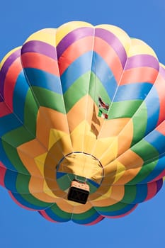 Colored hot-air balloon in flight seen from below against a blue sky