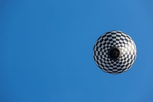 Black and white balloon in flight seen from below against a blue sky