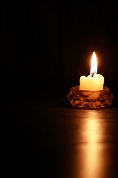 One lighting candle in glass candlestick against dark background